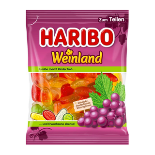 Haribo Weinland vingummier fra Købogspar – farverig pose med frugtvingummier formet som druer og vinregioner, vist i rød, gul, orange og grøn farve. Forsiden af posen er lilla med stor HARIBO-logo øverst og teksten ‘Weinland’ i gult. Nederst ses illustrationer af lilla vindruer og grønne blade. Den gennemsigtige del af posen viser vingummierne indeni. Produktet er perfekt til deling og kendt for frugtagtig smag. Købes hos Købogspar med hurtig levering, gode priser, stort udvalg og nem online bestilling. 